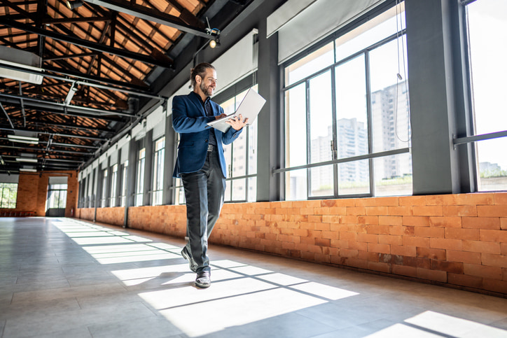 Man in suit holding a computer walking down a hallway in a commercial building